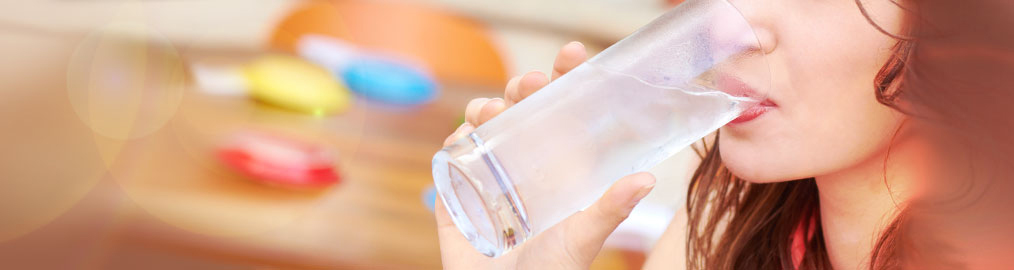 Woman drinking water in front of blurred pills